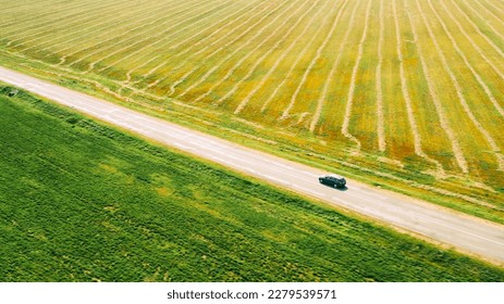 Elevated Aerial View Of Blue Car Vehicle Automobile In Fast Drive Motion On Countryside Country Road Through Green Fields. Agricultural Country Rural Landscape. Car Drive In Motion.
