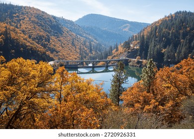 Elevated autumn view of Pit 3 Dam spanning Lake Britton, surrounded by colorful fall foliage and forested mountains in Shasta County, California.