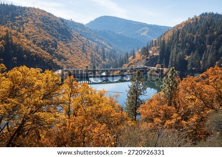 Elevated autumn view of Pit 3 Dam spanning Lake Britton, surrounded by colorful fall foliage and forested mountains in Shasta County, California.