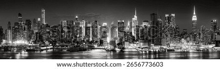 Elevated black and white panoramic view of Midtown Manhattan skyline at night with skyscrapers, Times Square lights, and reflections on the Hudson River. New York City, USA
