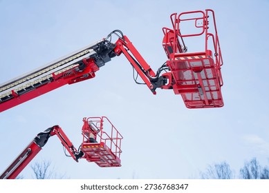 Elevated cherry picker baskets on red telescopic boom lifts reaching into blue sky, aerial work platform equipment for industrial building maintenance, repair and safety tasks