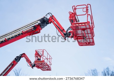 Elevated cherry picker baskets on red telescopic boom lifts reaching into blue sky, aerial work platform equipment for industrial building maintenance, repair and safety tasks