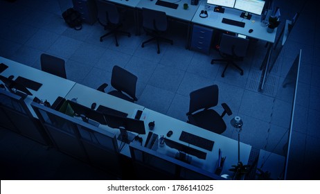 Elevated High Angle Shot Of Dark Empty Office With Wheelchairs, Desks And Computers. Concept Of Finishing Working Alone Late At Night.