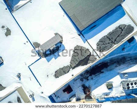 Elevated overhead drone view of a flat roofed building with snow load and ventilation units.