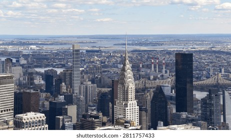 Elevated panoramic view across Midtown Manhattan featuring the iconic Chrysler Building, Queensboro Bridge and the New York City skyline beneath dramatic clouds. A classic commercial travel and architecture photograph.