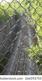 An elevated perspective, looking down through a chain-link fence onto a set of railway tracks.