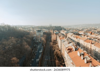 Elevated perspective of Prague showing rows of red rooftops, railway lines, and the pointed towers of Vyšehrad Basilica rising over tree-lined city streets