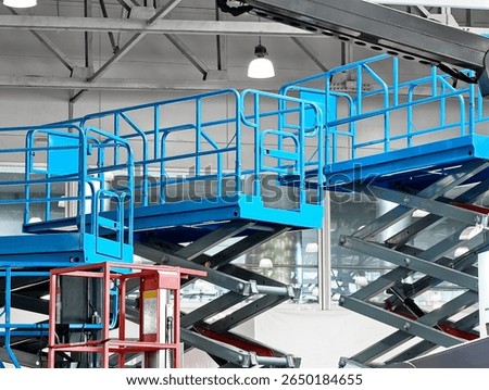Elevated platforms in a modern warehouse setting featuring blue and red scissor lifts during daylight hours