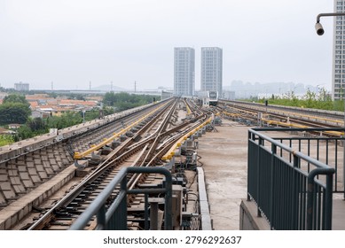 Elevated transit tracks with a train approaching and high-rise buildings under a hazy sky.