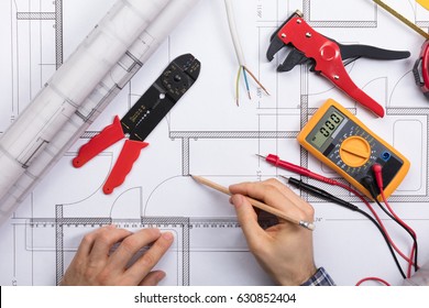 Elevated View Of An Architect Drawing Plan On Blueprint With Electrical Components