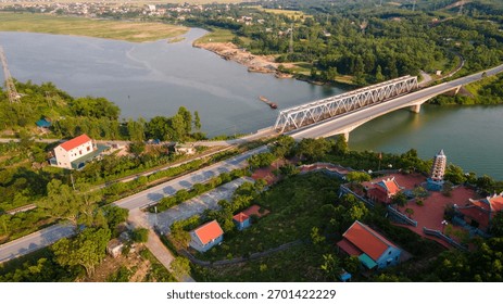 Elevated view of a bridge connecting a sparsely populated, forested riverbank with a more developed residential area. Illustrates themes of rural development and expansion.