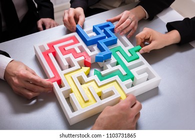 Elevated View Of Businesspeople Hand Solving Maze Puzzle On Desk In Office