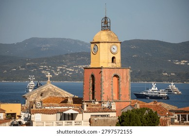 An elevated view from the citadel frames the bell tower above terracotta rooftops, with marina masts, yachts, blue bay water and wooded hills in the distance. Saint-Tropez, Var, Provence-Alpes-Cote d Azur, France