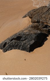 An elevated view of a cluster of reddish granite rocks on the golden sand of a beach.