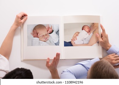 Elevated View Of Couple Looking At Baby's Photo Album On White Background