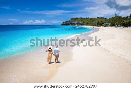 Elevated view of a couple walking down the beuatiful Darkwood beach with turquoise sea in the Caribbean, Antigua and Barbuda islands