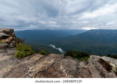 Elevated view of deep rugged valley and rolling hills from a rocky cliff edge. Gloomy day with dramatic cloudscape. White mist rising from the valley trough (mid-ground). - Powered by Shutterstock