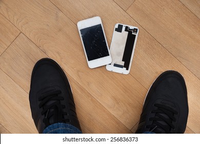 Elevated View Of Foot And Broken Cellphone On Hardwood Floor