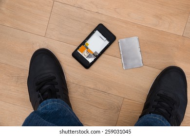 Elevated View Of Foot And Broken Cellphone On Hardwood Floor