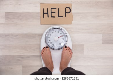 Elevated View Of Help Sign On Cardboard With Woman's Feet On Weighing Scale