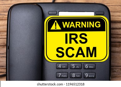 Elevated View Of IRS Scam Warning Sign On Black Landline Phone