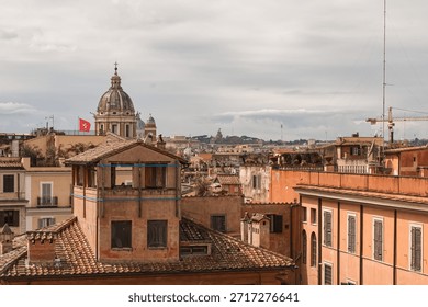 An elevated view looking down the busy Spanish Steps in Rome (Piazza di Spagna), showing a crowd of people around the fountain and the busy, wet street flanked by tall, historic buildings.