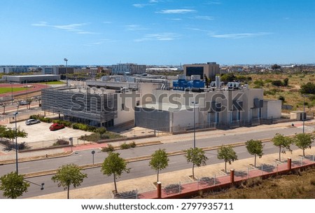 Elevated view of a modern data centre building with extensive rooftop HVAC and cooling tower infrastructure in an urban technology campus near sports facilities and city skyline, Spain