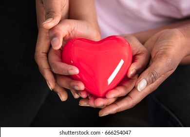 Elevated View Of Mother's And Daughter's Hand Holding Red Heart