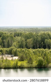 Elevated view over the emerald waters of Rummu Quarry, Estonia, bordered by lush mixed forest and Betula spp. birch trees under soft summer light.