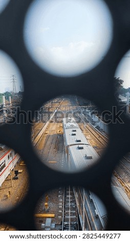 Elevated view of passenger trains and multiple railway tracks seen through circular openings in a dark metal structure.