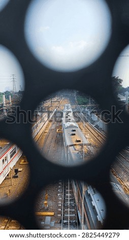 Elevated view of passenger trains and multiple railway tracks seen through circular openings in a dark metal structure.