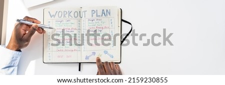 An Elevated View Of A Person Making Note Of Workout Plan On Notebook