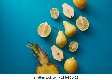 elevated view of pineapple, pears and lemons on blue surface