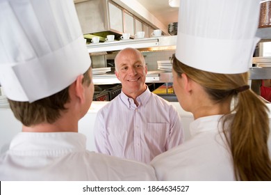 Elevated View Of A Restaurant Manager Talking To Male And Female Chefs In A Commercial Kitchen.