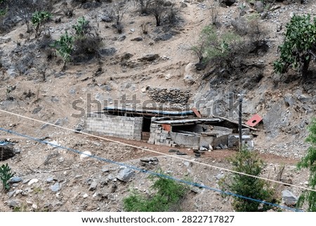 An elevated view of a rustic, small stone and brick outbuilding or shed located on a dry, rocky hillside in the mountainous landscape of Yunnan, China.