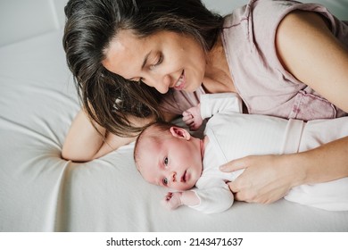 elevated view of smiling mother hugging cute newborn baby girl yawning at home. Family concept