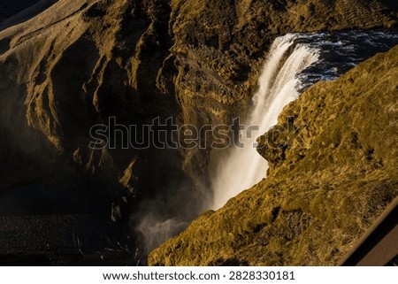Elevated view from the top cliff observation deck of Skógafoss waterfall, showing the power of the water cascading down into the deep, misty gorge below in Iceland.