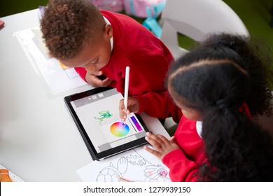 Elevated View Of Two Kindergarten School Kids Sitting At A Desk In A Classroom Drawing With A Tablet Computer And Stylus, Close Up