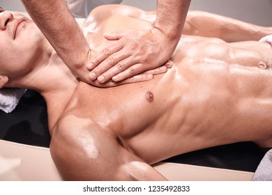 Elevated View, Two Young Man, 20-29 Years Old, Sports Physiotherapy Indoors In Studio, Photo Shoot. Masseur Massaging Athlete Mans Chest, Muscular Body, Hands Close-up.