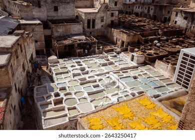 An elevated, wide-angle view captures the bustling Chouara Tannery in Fes, Morocco, with numerous stone vats filled with various colored dyes and hides, surrounded by traditional multi-story buildings