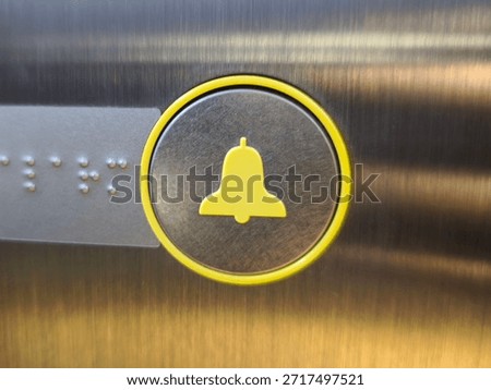 An elevator alarm button featuring a yellow bell icon, a matching circular border, and adjacent tactile Braille lettering.