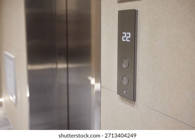 Elevator control panel displaying floor , brushed steel doors, beige wall, illuminated numeric display, round tactile buttons, soft ambient corridor lighting,