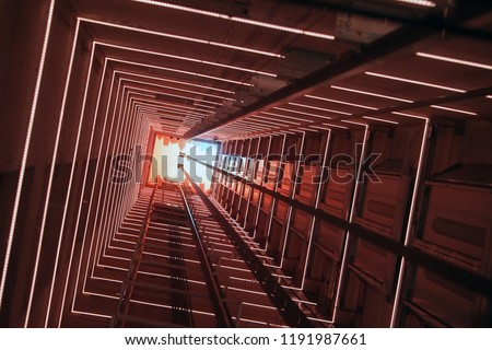 Elevator corridor in the building lit by red elumination. Futuristic elevator shaft is located in a high tower. Lift shaft in a residential building. Abstract, background. Bottom view.