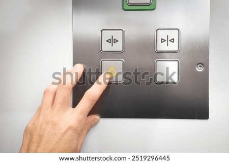 Elevator emergency call button used by passenger. Close up of woman pushing a button with a bell icon on stainless steel intercom. Call for help or stuck elevator in building. Selective focus.