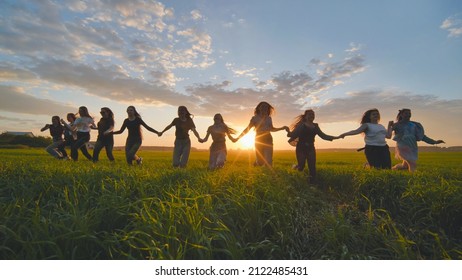 Eleven cheerful girls run to the meeting across the field in the summer, holding hands.