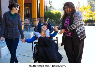 Eleven year old biracial disabled boy in wheelchair holding hands with caregivers while on a walk outdoors