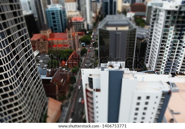 Elevted view of\
city with church and buildings in minature effect. Main roda with\
cars lined by trees. Tall buildings office and residental\
apartments surround the church and\
road.