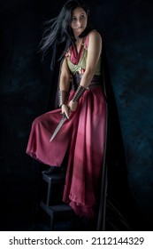 An Elf Warrior Queen Wearing A Laced Bodice And Draped Skirt With A Cloak And Holding A Dagger