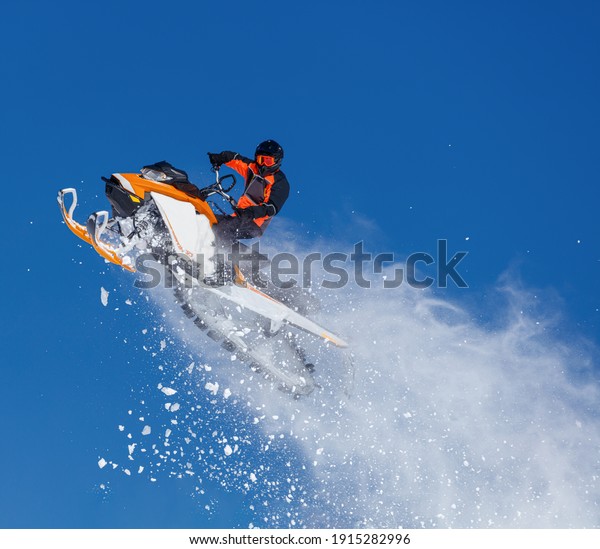 elite sports snowmobiler rides and jumps on steep
mountain slope with swirls of snow storm. background of blue sky
leaving a trail of splashes of white snow. bright snowmobile and
suit without brands