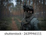 An elite unit soldier in full tactical gear and a helmet with a night vision device conducts surveillance during a patrol in the forest.